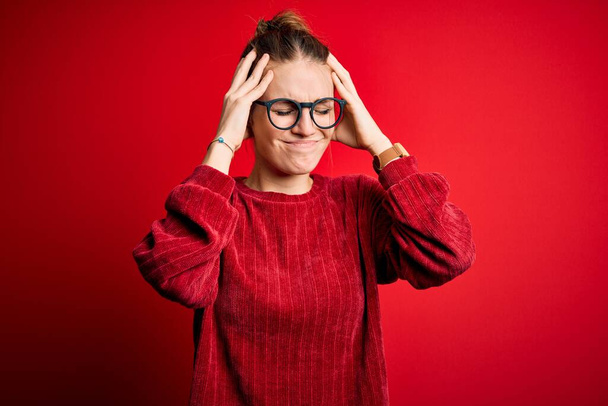 Young beautiful redhead woman wearing casual sweater over isolated red background suffering from headache desperate and stressed because pain and migraine. Hands on head. - Photo, Image