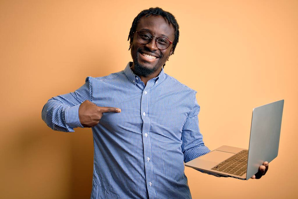 Genç Afro-Amerikan işçi dizüstü bilgisayarla çalışıyor sarı arka planda durup kendini işaret ediyor. - Fotoğraf, Görsel