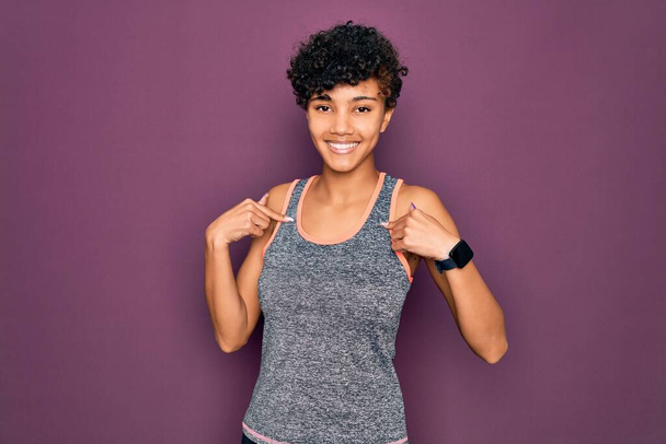 Joven hermosa afroamericana afro deportista haciendo ejercicio usando ropa deportiva buscando confiado con sonrisa en la cara, señalándose con los dedos orgullosos y felices
. - Foto, Imagen