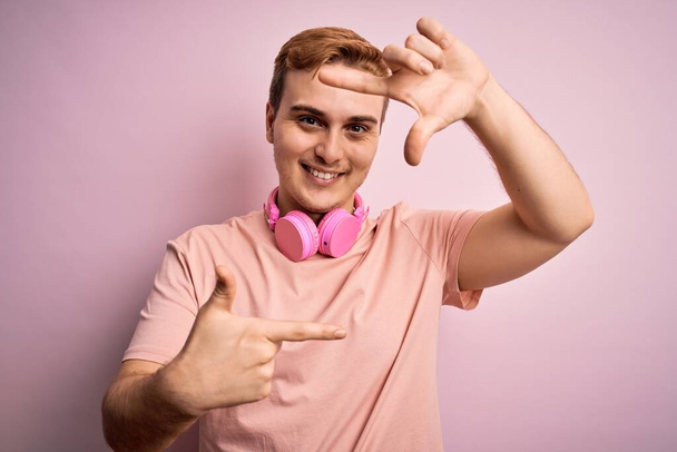 Giovane bell'uomo rossa che ascolta musica usando le cuffie su sfondo rosa sorridendo facendo cornice con le mani e le dita con il viso felice. Creatività e concetto di fotografia
. - Foto, immagini