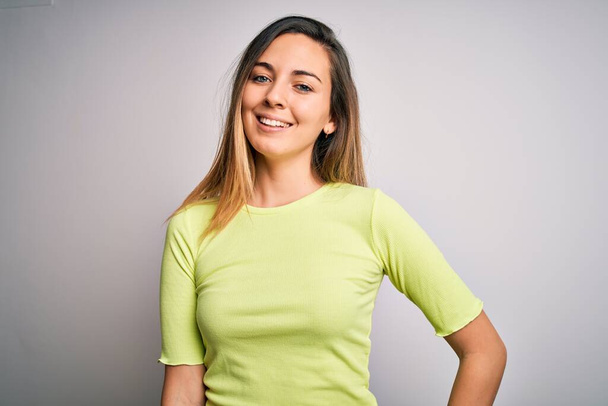 Beautiful blonde woman with blue eyes wearing green casual t-shirt over white background with a happy and cool smile on face. Lucky person. - Fotoğraf, Görsel