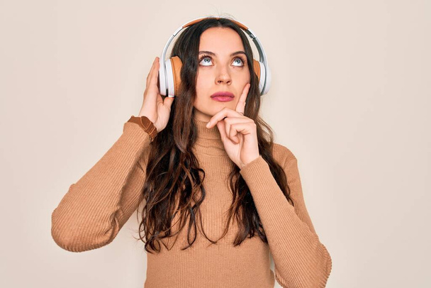 Young beautiful woman with blue eyes listening to music and dancing using headphones serious face thinking about question, very confused idea - Foto, immagini