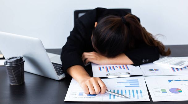 Financial accountant works on analyzing and summarizing the company's incomes and expenses in real estate and account management, causing her to get tired and fall asleep on her desk, Hard work and overtime work concept. - Foto, Bild