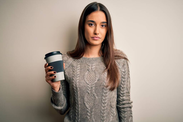 Молодая красивая брюнетка женщина пьет кофе на изолированном белом фоне с уверенным выражением на умном лице, думая серьезно
 - Фото, изображение