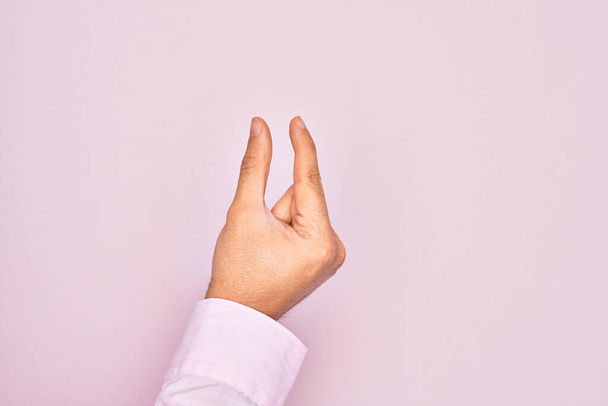 Hand of caucasian young man showing fingers over isolated pink background picking and taking invisible thing, holding object with fingers showing space - Photo, Image