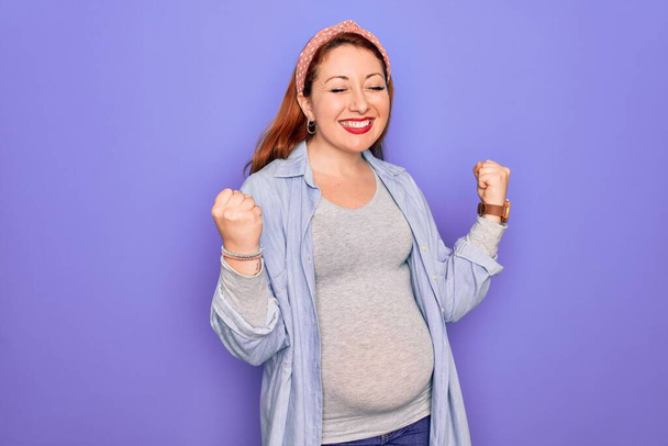 Young beautiful redhead pregnant woman expecting baby over isolated purple background excited for success with arms raised and eyes closed celebrating victory smiling. Winner concept. - Photo, Image