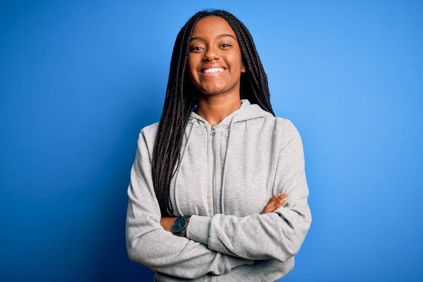 Jovem atleta afro-americana vestindo camisola esportiva sobre fundo azul isolado rosto feliz sorrindo com os braços cruzados olhando para a câmera. Pessoa positiva
. - Foto, Imagem