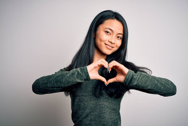 Young beautiful chinese woman wearing casual t-shirt over isolated white background smiling in love showing heart symbol and shape with hands. Romantic concept. - Foto, imagen