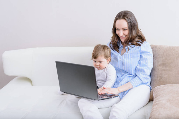 Lächelnde Mutter mit Kind, die auf der Couch sitzt und sich Cartoons auf dem Laptop ansieht, glückliche Mutterschaft, Mutterschaft, langsames Lebenskonzept - Foto, Bild