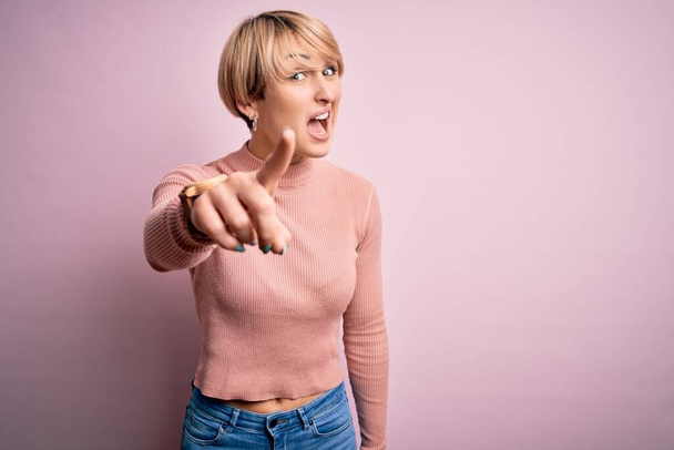 Young blonde woman with short hair wearing casual turtleneck sweater over pink background pointing displeased and frustrated to the camera, angry and furious with you - Photo, Image