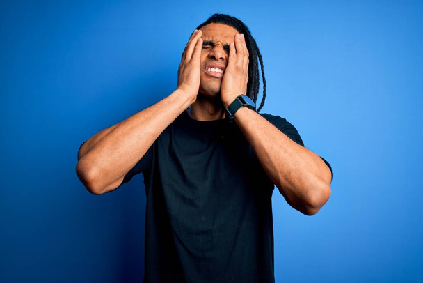 Jeune homme afro afro afro américain beau avec dreadlocks portant t-shirt décontracté souffrant de maux de tête désespérés et stressés parce que la douleur et la migraine. Mains sur la tête
. - Photo, image