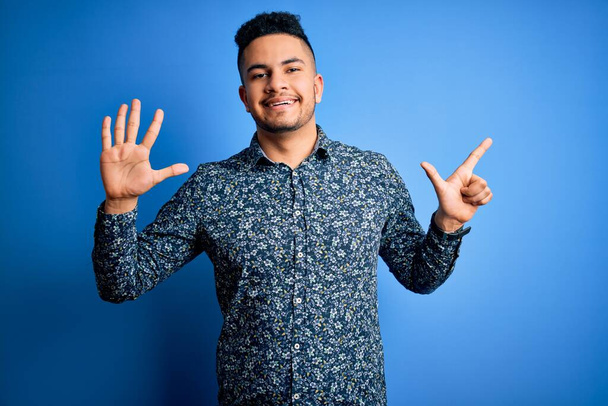 Fiatal jóképű férfi alkalmi ing áll az elszigetelt kék háttér mutatja, és rámutatva ujjak száma 7 miközben mosolygós magabiztos és boldog. - Fotó, kép