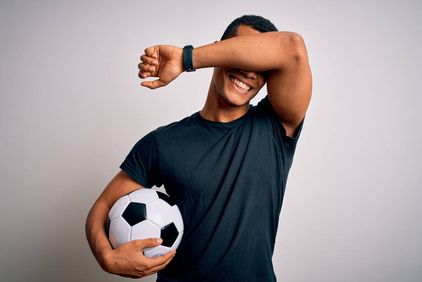 白い背景の上でサッカーボールを持ってサッカーをしているハンサムなアフリカ系アメリカ人の男性明るい顔を示す手で竹を覗かせる笑顔。驚きと興奮した - 写真・画像