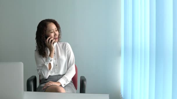 Asian Chinese Businesswoman talking and arguing on the cellphone. Sitting next to her office windows. - Záběry, video