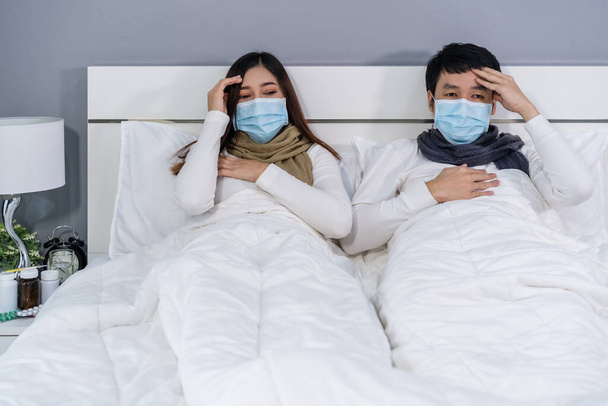 sick couple in medical mask headache and suffering from virus disease and fever in a bed, coronavirus (covid-19) pandemic concept. - Φωτογραφία, εικόνα