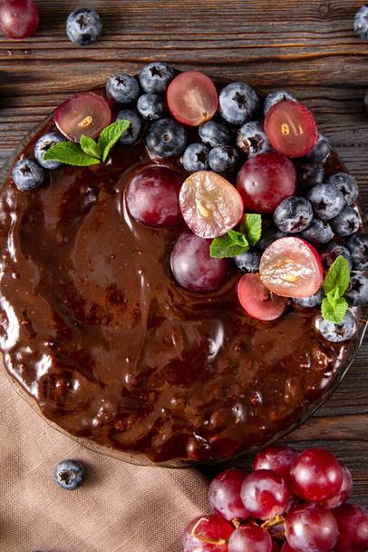homemade chocolate cake with fresh berries red grapes and blueberries, mint on a beige towel on a wooden brown background, berry pie close up, baking - Fotografie, Obrázek