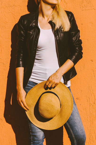 lower body of young woman in black jacket white t shirt and hat in hands lean on yellow wall in city summer hot day - Foto, Imagem