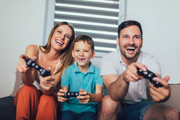 Счастливая семья играет дома в видеоигры и веселится вместе. - Фото, изображение