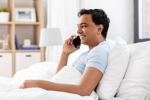 happy indian man calling on smartphone in bed - Foto, afbeelding