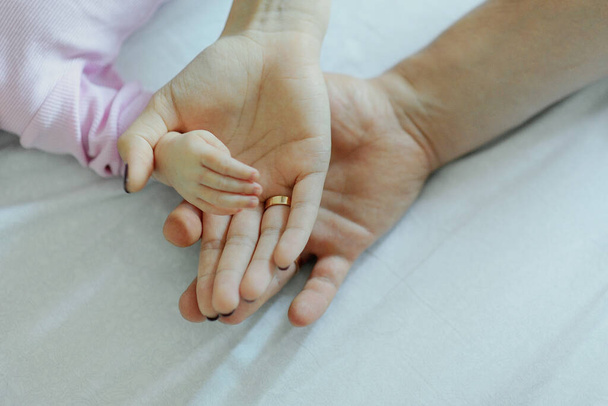Isä, äiti ja vauva pitävät toisiaan kädestä. Kaikkien perheenjäsenten kämmenet. Isä ja äiti pitävät vastasyntyneen vauvan kahvaa kämmenissä
 - Valokuva, kuva