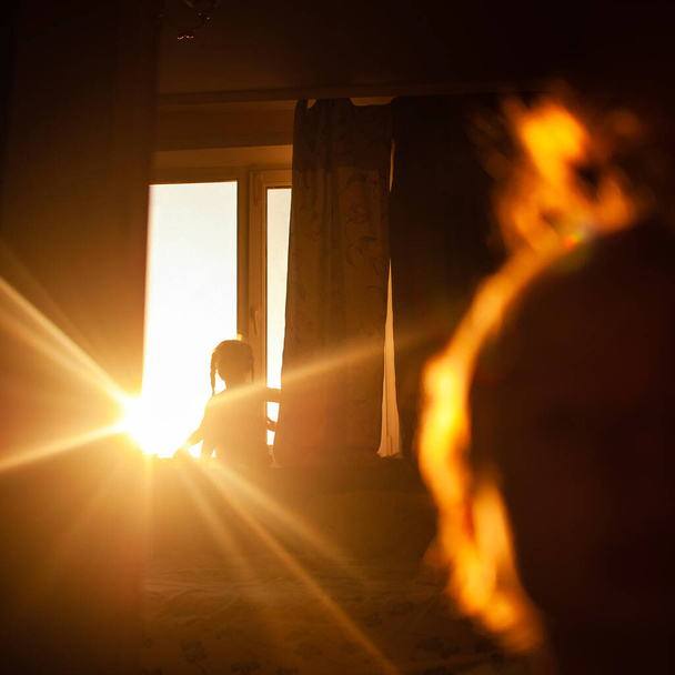 lapset leikkivät huoneessa auringonlaskun säteiltä. Pienet lapset kotona taustavalossa. Aurinko paistaa ikkunan läpi lasten taustalla. Siluetti materiaalia lasten kotona säteet laskevan auringon
. - Valokuva, kuva