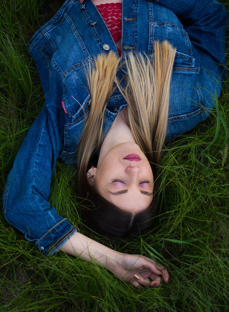  Girl with beautiful hair lying on her back in the green, juicy grass. Warm spring evening - Fotografie, Obrázek