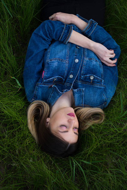  Girl with beautiful hair lying on her back in the green, juicy grass. Warm spring evening - Φωτογραφία, εικόνα