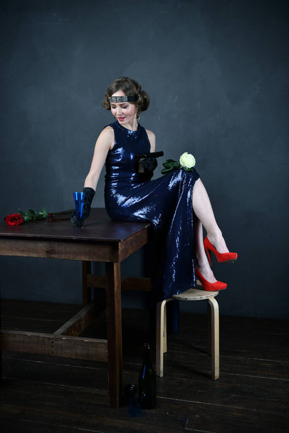 schöne Frau im blauen Abendkleid in schwarzen Handschuhen sitzt auf einem Tisch mit einem Gewehr - Foto, Bild