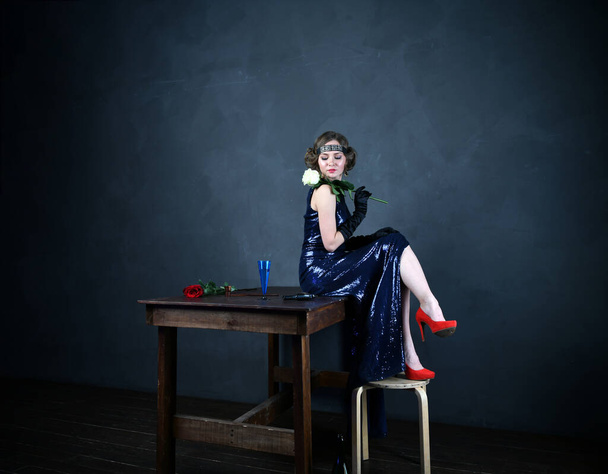 όμορφη γυναίκα σε ένα μπλε βραδινό φόρεμα σε μαύρα γάντια κάθεται σε ένα τραπέζι - Φωτογραφία, εικόνα
