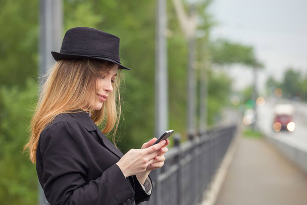Portrét krásné mladé ženy s mobilním telefonem na ulicích města. Módní fotka. - Fotografie, Obrázek