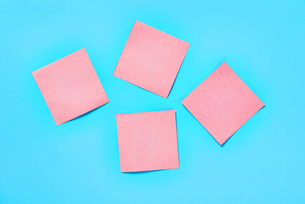 Four pink square blank paper stickers on blue background. Copy space. Top view - Foto, immagini