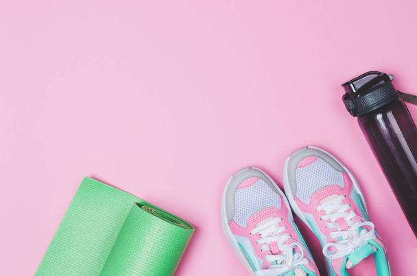 Tappetino yoga, scarpe sportive, bottiglia d'acqua su sfondo rosa. Uno stile di vita sano. Copia spazio - Foto, immagini