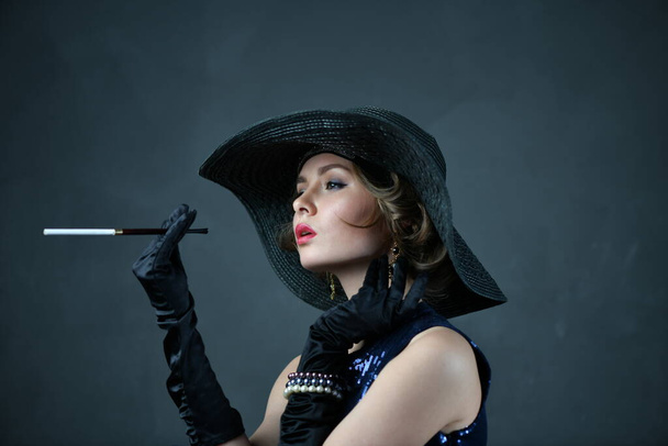 Siyah eldivenli, siyah şapkalı, piposu olan mavi elbiseli güzel bir kadın. - Fotoğraf, Görsel