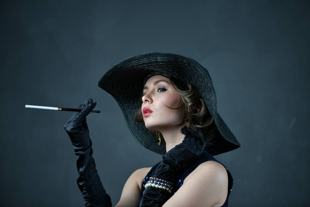 bella donna in abito da sera blu con guanti neri e un cappello nero e una pipa
 - Foto, immagini
