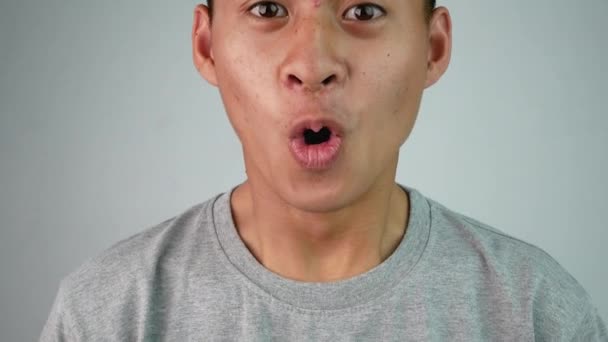 Aziatisch tiener guy in grijs t-shirt enthousiast en verrassing met wat hij zag in de voorkant, geïsoleerd op grijze achtergrond. - Video