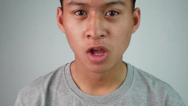 Asiatischer Teenager im grauen T-Shirt aufgeregt und überrascht mit dem, was er vor sich sah, isoliert auf grauem Hintergrund. - Filmmaterial, Video