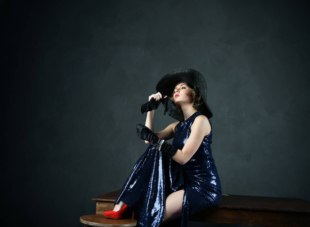 beautiful woman in a blue evening dress in black gloves and a black hat and with a gun - Foto, Imagem