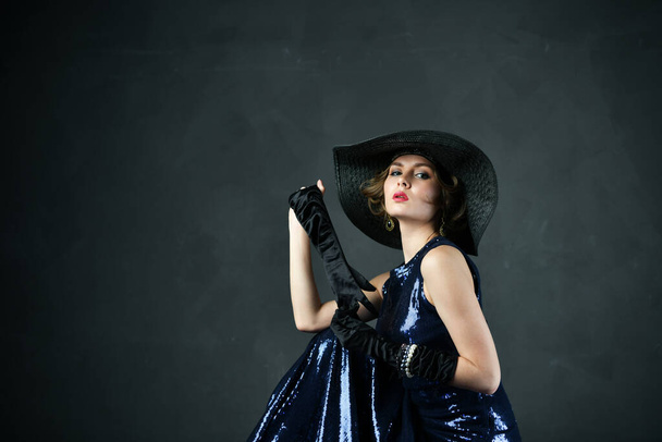 bela mulher em um vestido de noite azul em luvas pretas e um chapéu preto e com uma arma
 - Foto, Imagem