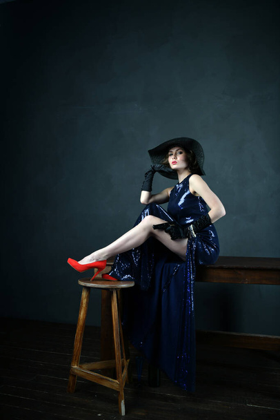 gyönyörű nő kék estélyi ruhában fekete kesztyűben és fekete kalapban és fegyverrel - Fotó, kép