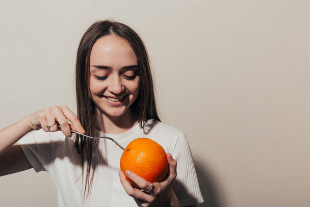 κορίτσι με όρεξη κοιτάζει ένα πορτοκάλι σε ένα πιρούνι.  - Φωτογραφία, εικόνα