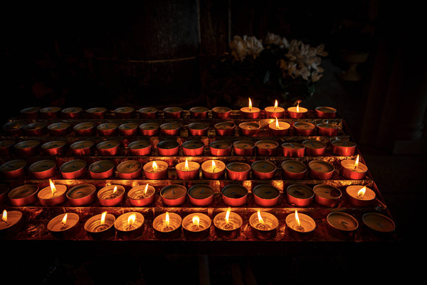 Closeup of votive candles, tea lights, in a dark Christian church. Italy, Europe - Photo, Image