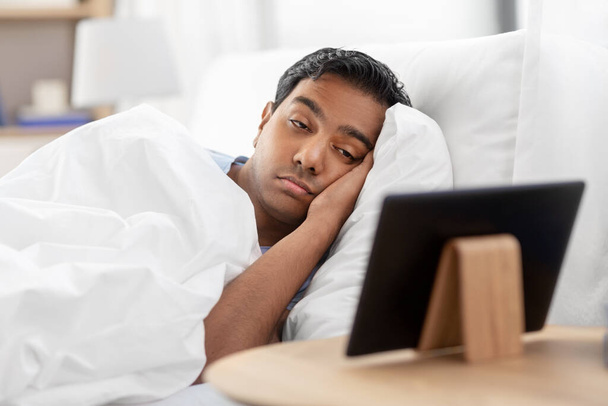 sleepy indian man looking at tablet pc in bed - Photo, Image
