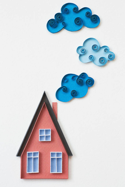 青い窓、白い背景に雲と赤い紙の家。白い背景にキルティング技術で作られた小さな家。紙の冷却技術で作られた手。家にいて。ホーム甘い家. - 写真・画像