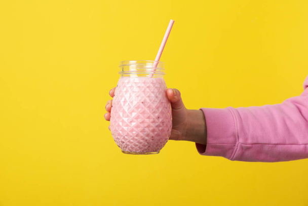 Woman holds glass of strawberry milkshake on yellow background - Photo, Image