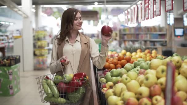 Richtige Ernährung, junges gesundes Mädchen mit Korb mit frischem Gemüse und Obst wählt Äpfel im Supermarkt - Filmmaterial, Video