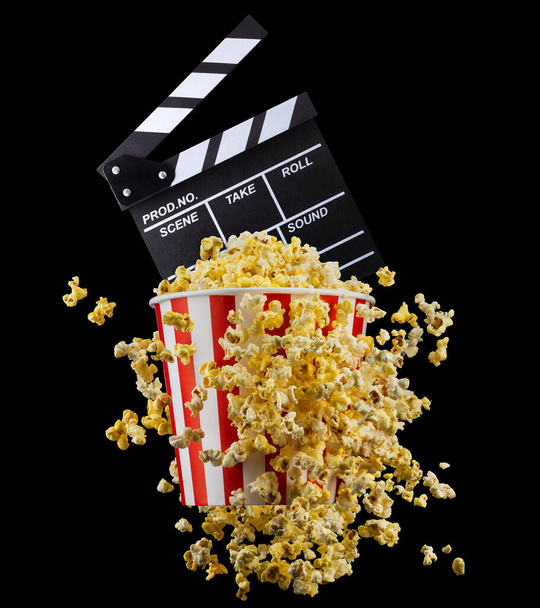 Flying popcorn and film clapper board isolated on black background, concept of watching TV or cinema. - Photo, Image