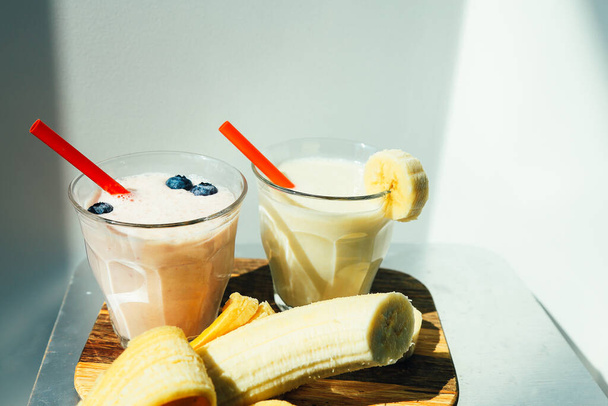 Due bicchieri di frullato di mirtillo di banana o frullato con paglia da bere e banana su sfondo bianco
 - Foto, immagini