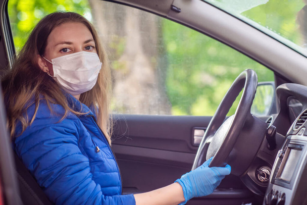 A woman driving a car in a protective medical mask and gloves. Lifestyle and safe drive during a pandemic coronavirus in quarantine. Protect the driver and passengers. New normal and modern reality - Fotoğraf, Görsel