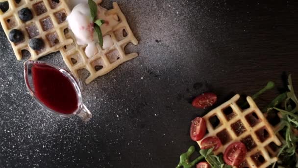 Presentation Fresh baked Belgian waffles with arugula, tomatoes, avocado and waffles topped with icecream, fresh blueberries and mint on black a plate. Savory waffles. Breakfast concept. Making food top view. - Filmagem, Vídeo