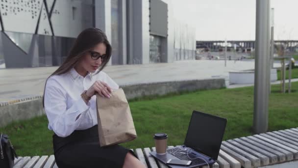 Mujer de negocios exitosa comiendo un croissant y tomando café al aire libre a la hora del almuerzo
 - Metraje, vídeo